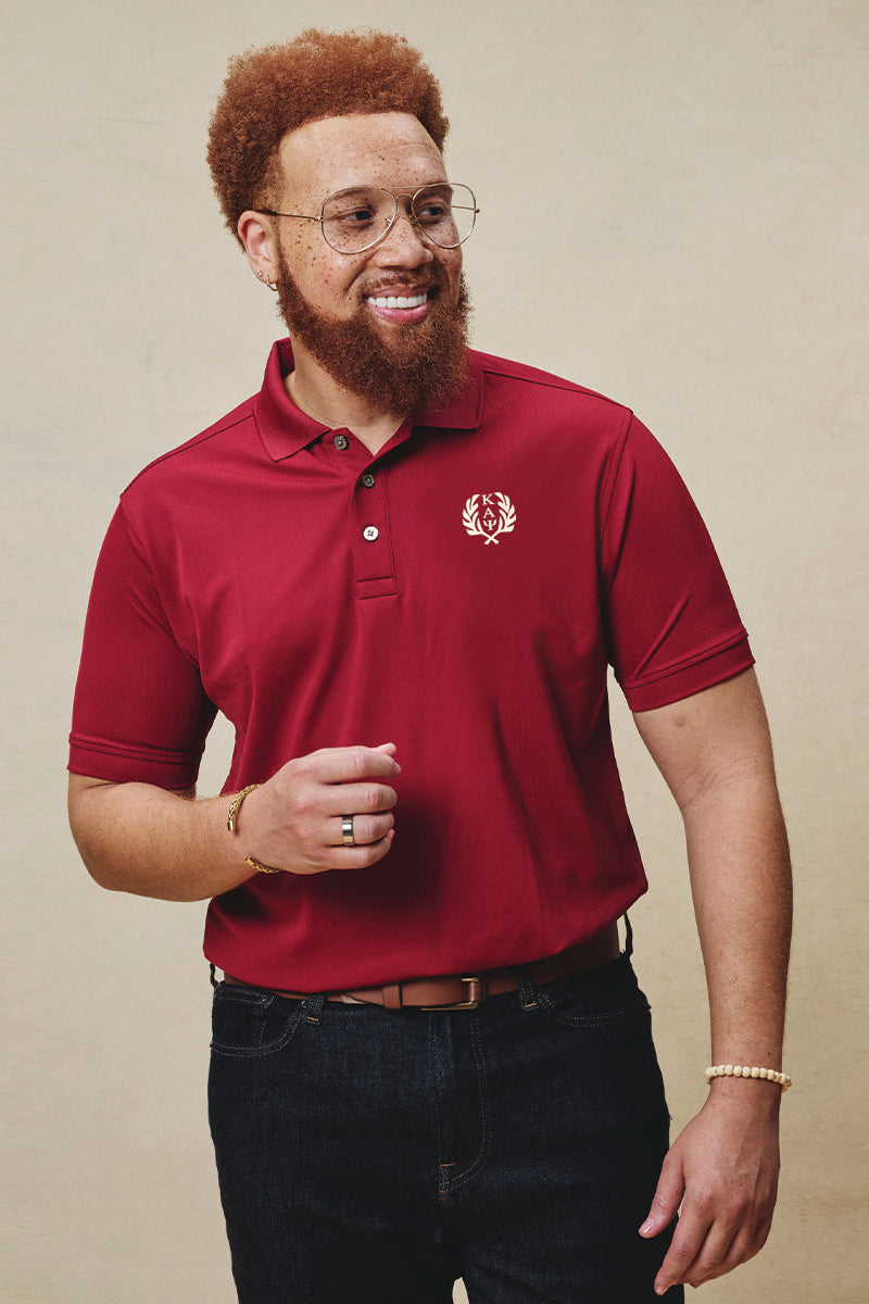 A man wearing a red Dri-fit polo shirt with the Kappa Alpha Psi fraternity's Greek letter wreath embroidered on the left chest.