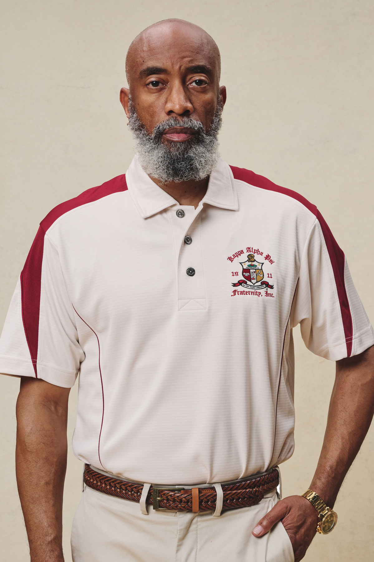 A man wearing a cream and krimson colored polo shirt with Kappa Alpha Psi Coat of Arms embroidery on the chest.